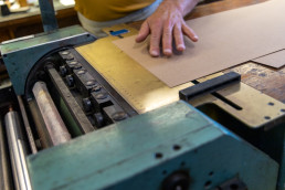 Hand operating vintage printing press with yellow ruler guide and paper sheet for Enaena project in teal and natural wood ton