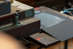 Letterpress printing setup with gray paper being pressed by green vintage press machinery, showing traditional printing proce