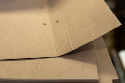Logo embossed on kraft paper envelope with warm beige tones and geometric fold lines creating dimensional shadows