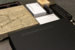 Black business cards with white text displaying Enaena contact details, arranged on wooden surface with white card stack