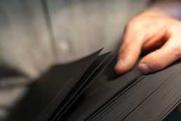 Hand touching black textured portfolio pages with soft focus background, showing tactile paper design for Enaena branding mat