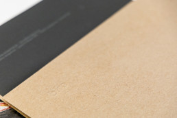 Brown kraft paper sheet with diagonal edge against dark gray surface, showing natural paper texture and fibers