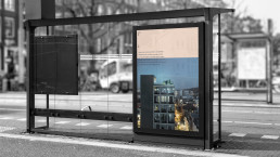 Modern glass bus stop shelter with colorful Enaena poster displaying urban apartment building and gradient blue-pink design