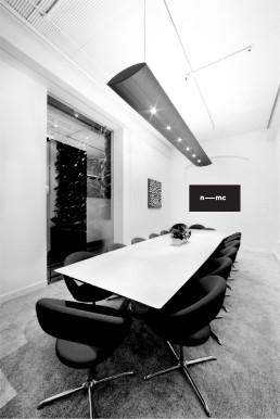 Modern black and white conference room with white table, black chairs, nmc logo on wall, and contemporary ceiling lighting.