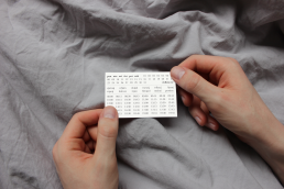 Hands holding a white schedule card with calendar dates and time slots against gray fabric background for domasi