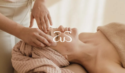 Logo for domasi overlaid on spa facial massage scene with therapist's hands treating client in soft beige tones