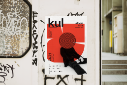 Poster mockup for kul abonma featuring bold red design with black concentric circles and silhouette, displayed on urban wall