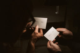 Business cards being exchanged between two hands in dramatic lighting, showcasing minimalist white card design for Lovro Rozi