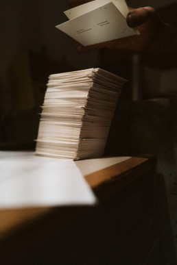 Mockup of stacked white paper documents with hand holding additional pages, warm lighting creates shadows across the scene