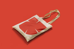 Canvas tote bag mockup with red geometric logo design on coral red background for kul abonma 2023