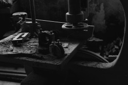 Black and white photograph showing vintage industrial machinery with heavy metal components, gears, and mechanical parts in d
