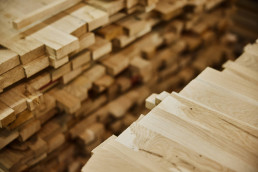 Stacks of light wooden lumber and timber boards arranged in a lumber yard, showing natural wood grain textures and warm beige