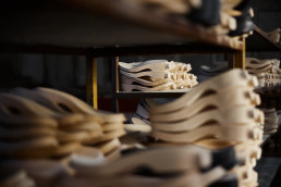 Wooden shoe forms and lasts organized on shelves in a cobbler's workshop, showing traditional shoemaking tools in warm brown