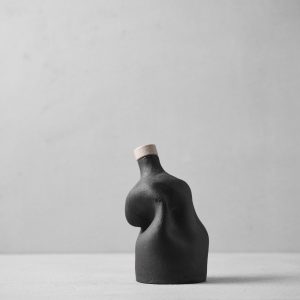 Dark ceramic bottle with cork stopper featuring organic curved form, minimal modern design on neutral background