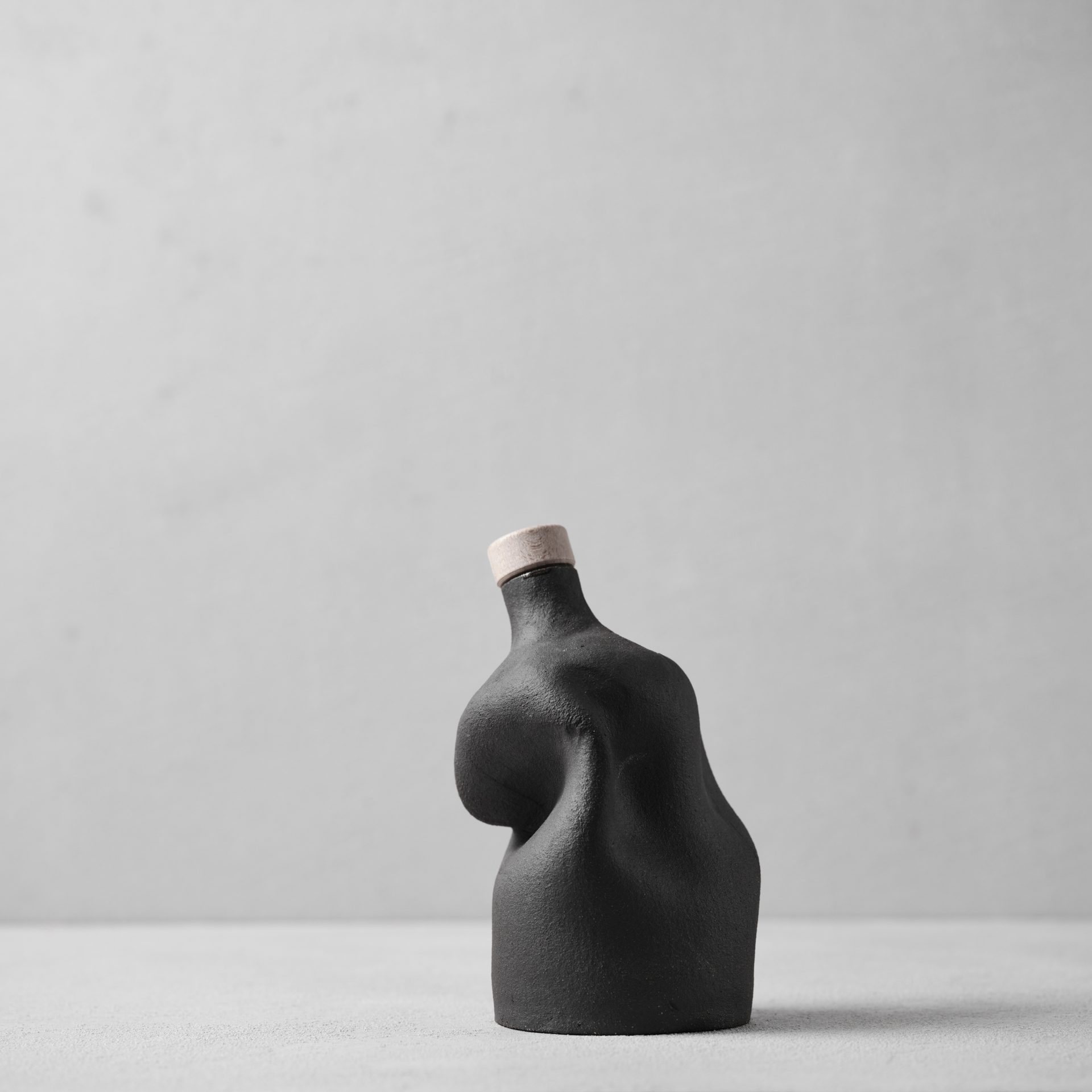 Dark ceramic bottle with cork stopper featuring organic curved form, minimal modern design on neutral background