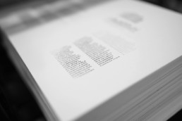 Black and white photograph of an open book showing two columns of text on white pages, with soft focus and artistic depth of