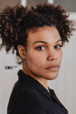 Professional headshot of woman with curly hair wearing black shirt for European Actors portfolio, clean white background