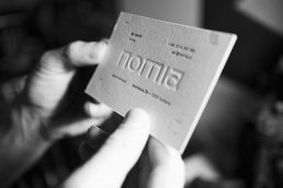 Black and white photo showing hands holding a white business card with embossed 