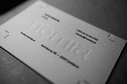 Business card mockup for nomia featuring embossed white logo and text on white paper with contact details and website